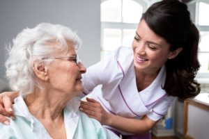 Smiling Nurse And Old Woman Patient At Wheelchair