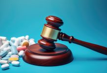 Een houten rechtershamer op een standaard, omringd door een verscheidenheid aan kleurrijke medicinale pillen en capsules, tegen een effen blauwe achtergrond, symboliseert de relatie tussen wetgeving en medicatie